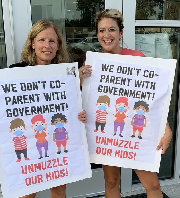 2 NPA women protesting mask mandates with signs reading We dont co-parent with the government, unmuzzle our kids